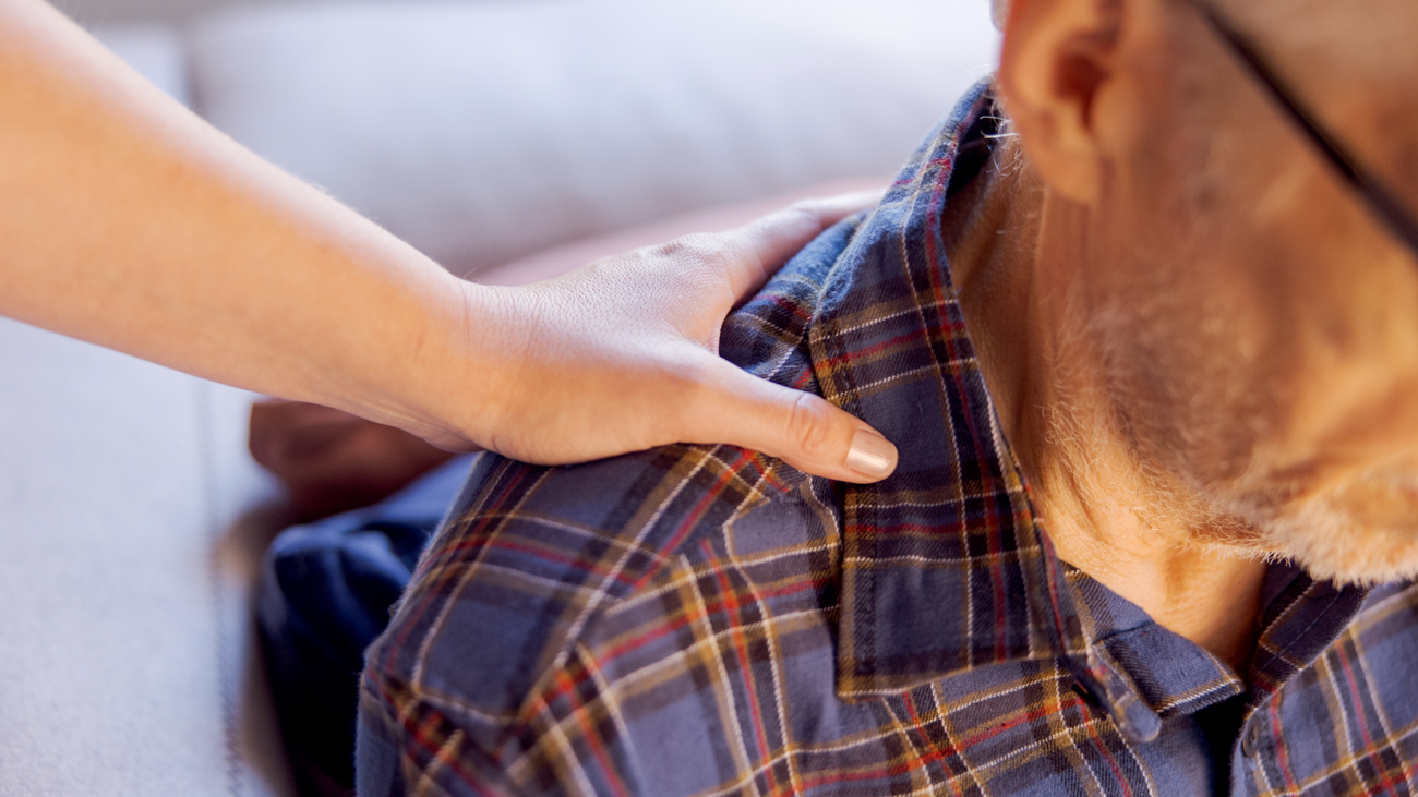 Close-up of a caring hand on an old man's shoulder.